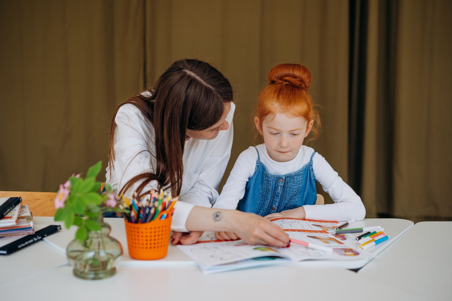 Teacher helps young girl with learning activity in a classroom setting, fostering education.