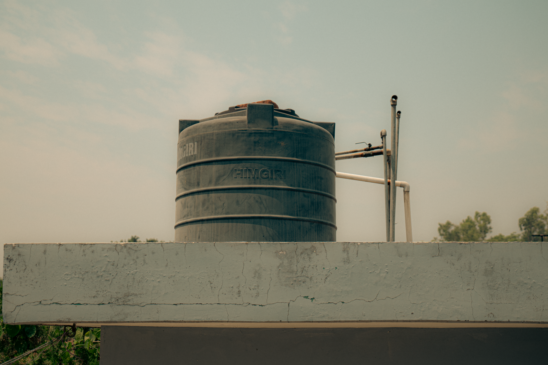 A black water storage tank placed on a rooftop with pipes, under a clear sky.