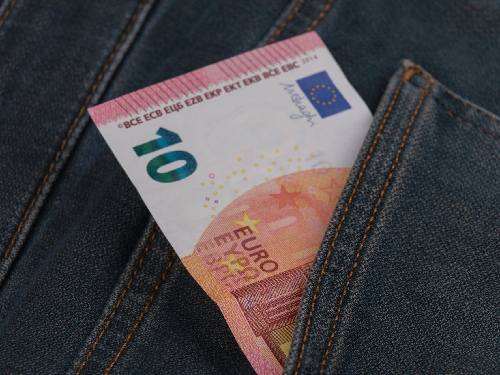 Close-up of a 10 euro banknote sticking out from a denim pocket.