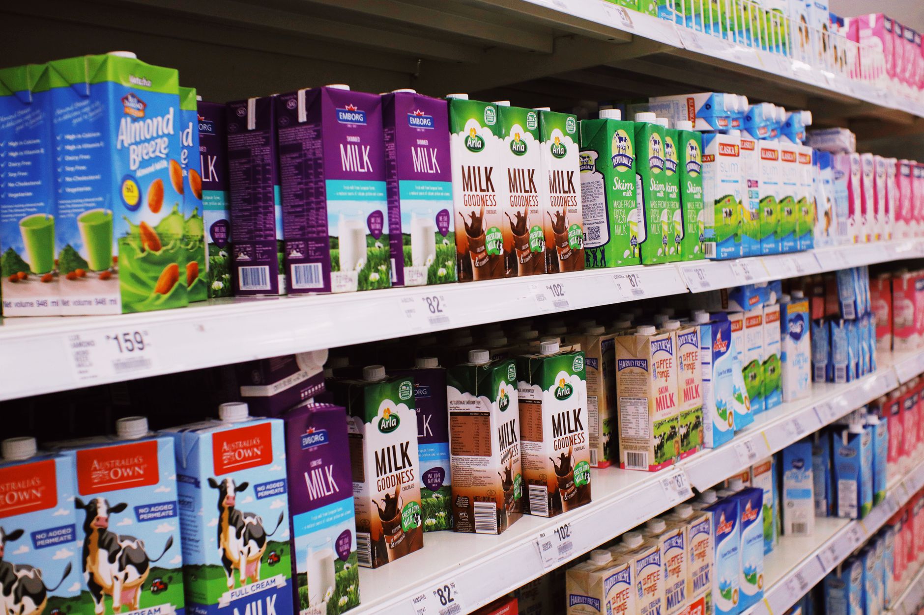 Various colorful boxes of milk placed on shelves with prices in modern supermarket