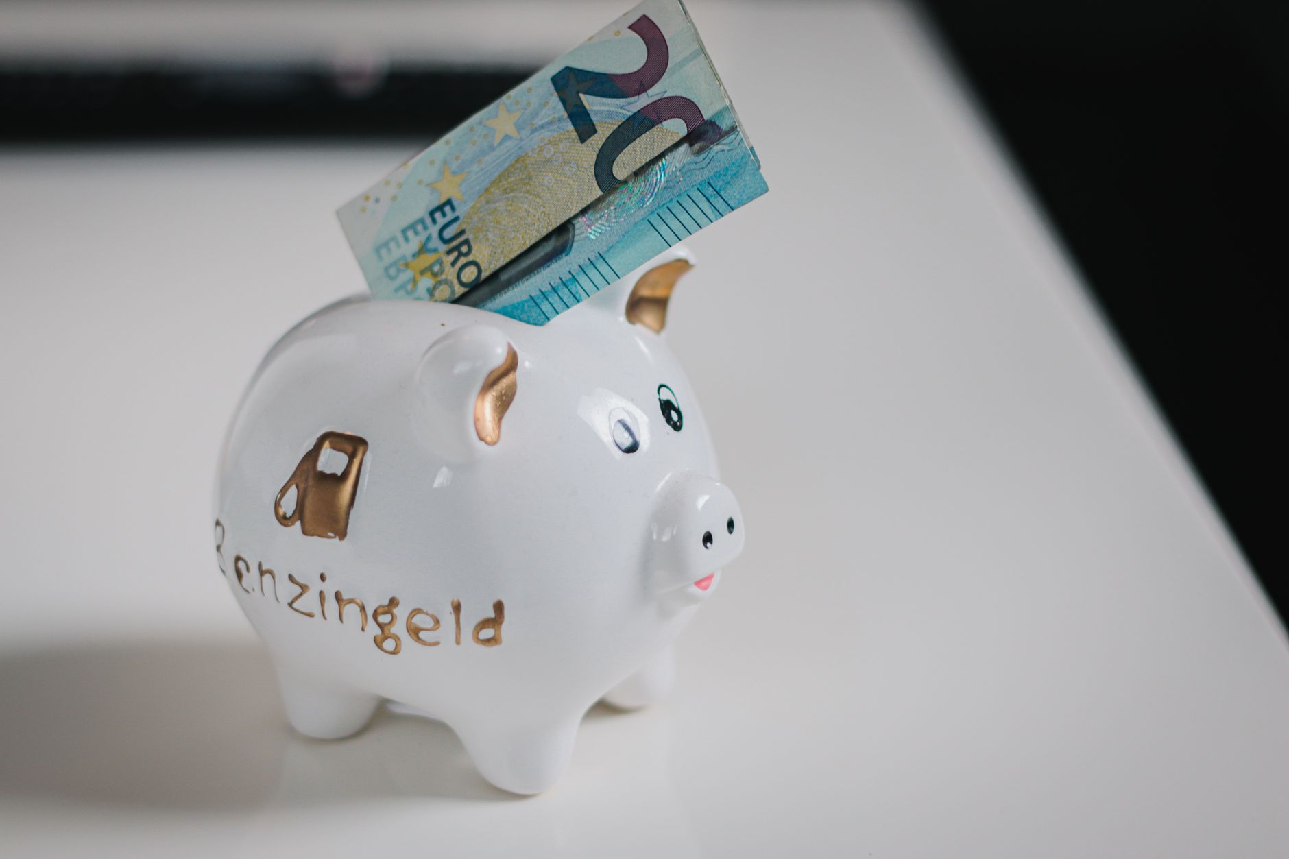 A white piggy bank with a €20 note inserted, symbolizing savings.