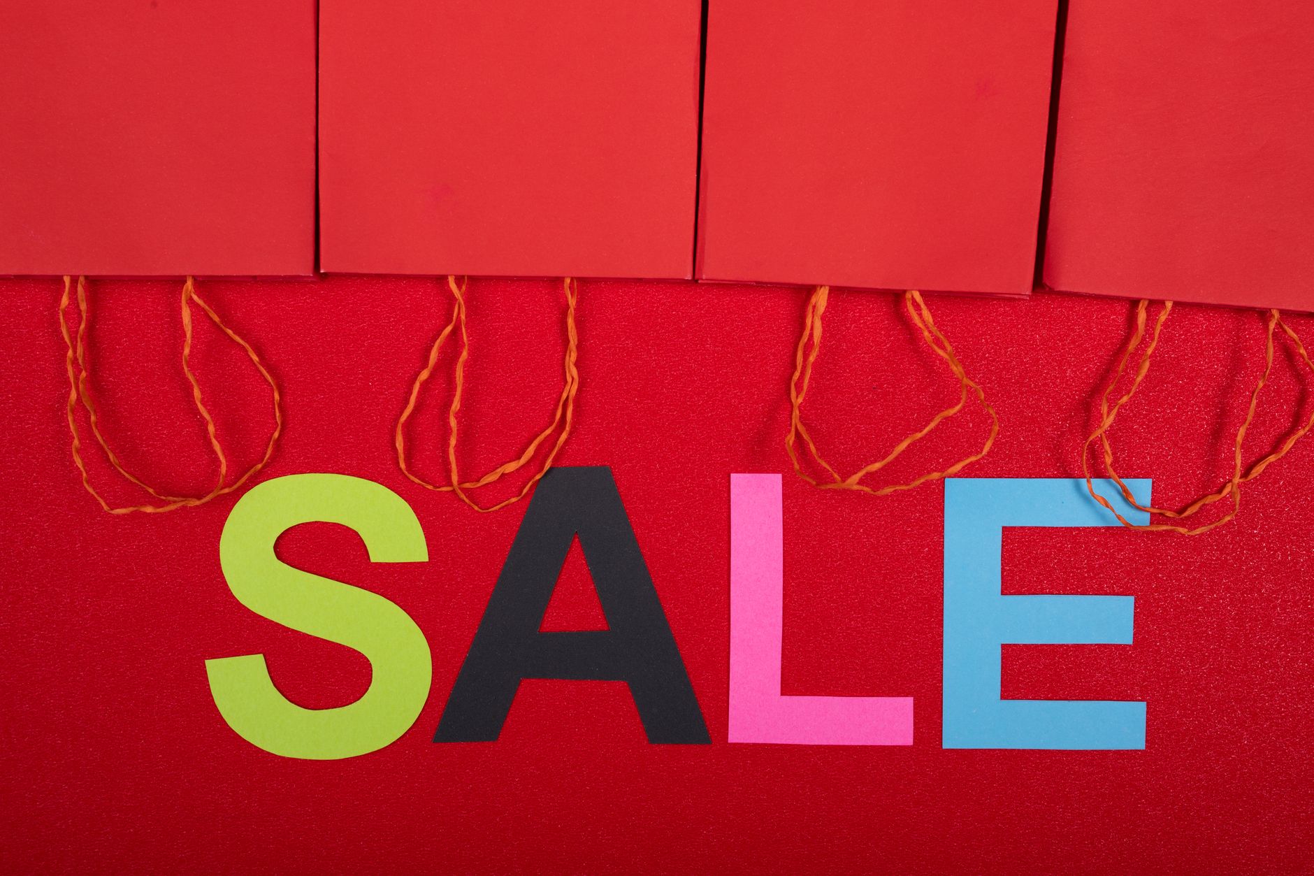 Colorful sale sign with red shopping bags for retail promotions.