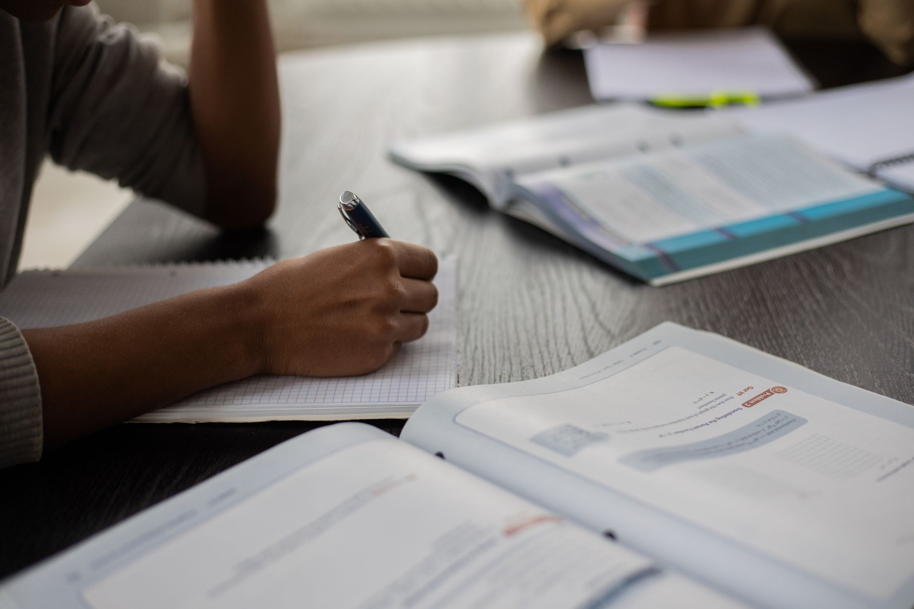 Side view of unrecognizable African American student sitting at table with textbooks while taking note in copybook in classroom with anonymo