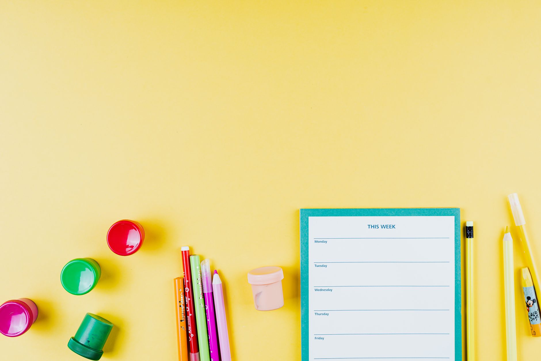 Flat lay of colorful school supplies on a yellow background with planner