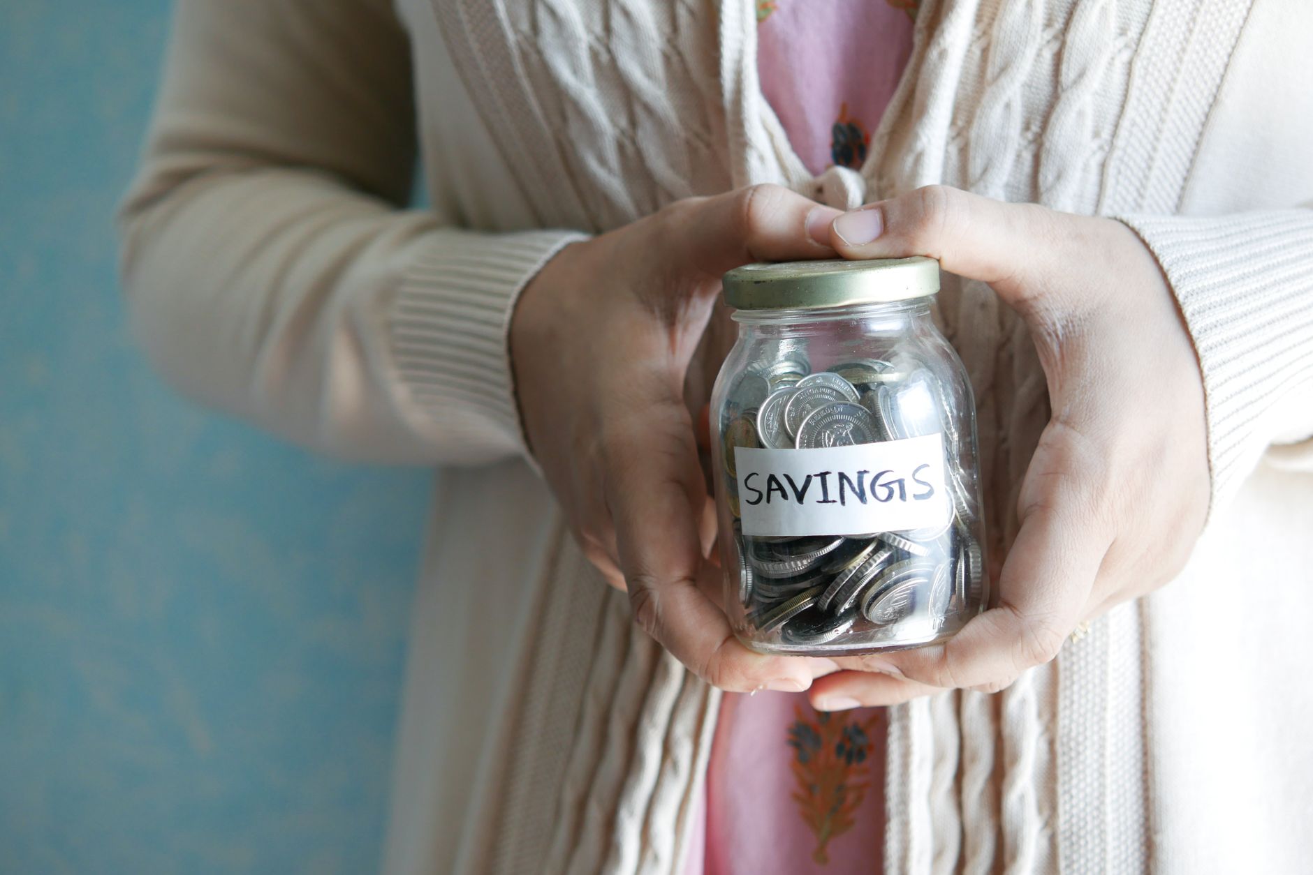 Woman holding a jar labeled 'savings' filled with coins, representing financial savings.