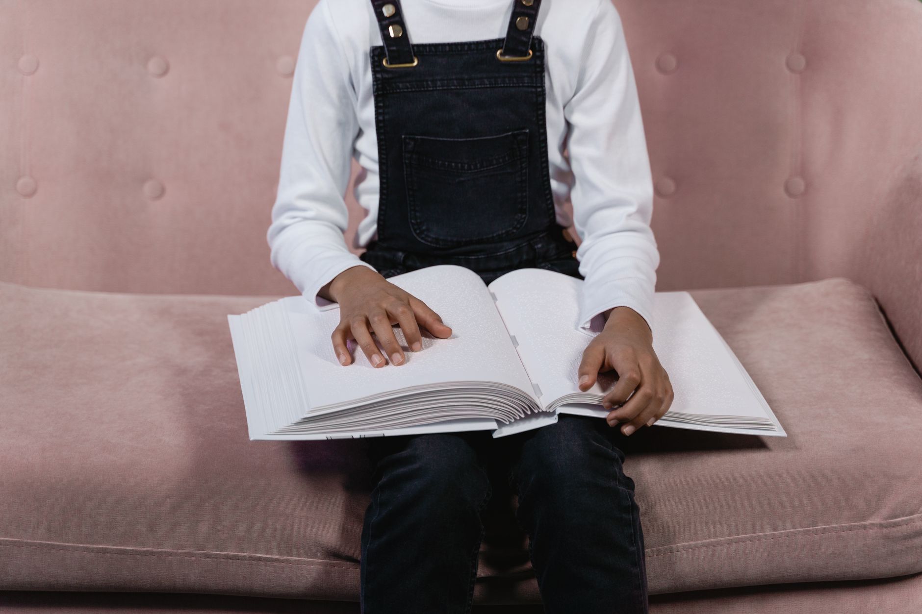 A child sits on a sofa holding and reading a Braille book, signifying learning and accessibility.