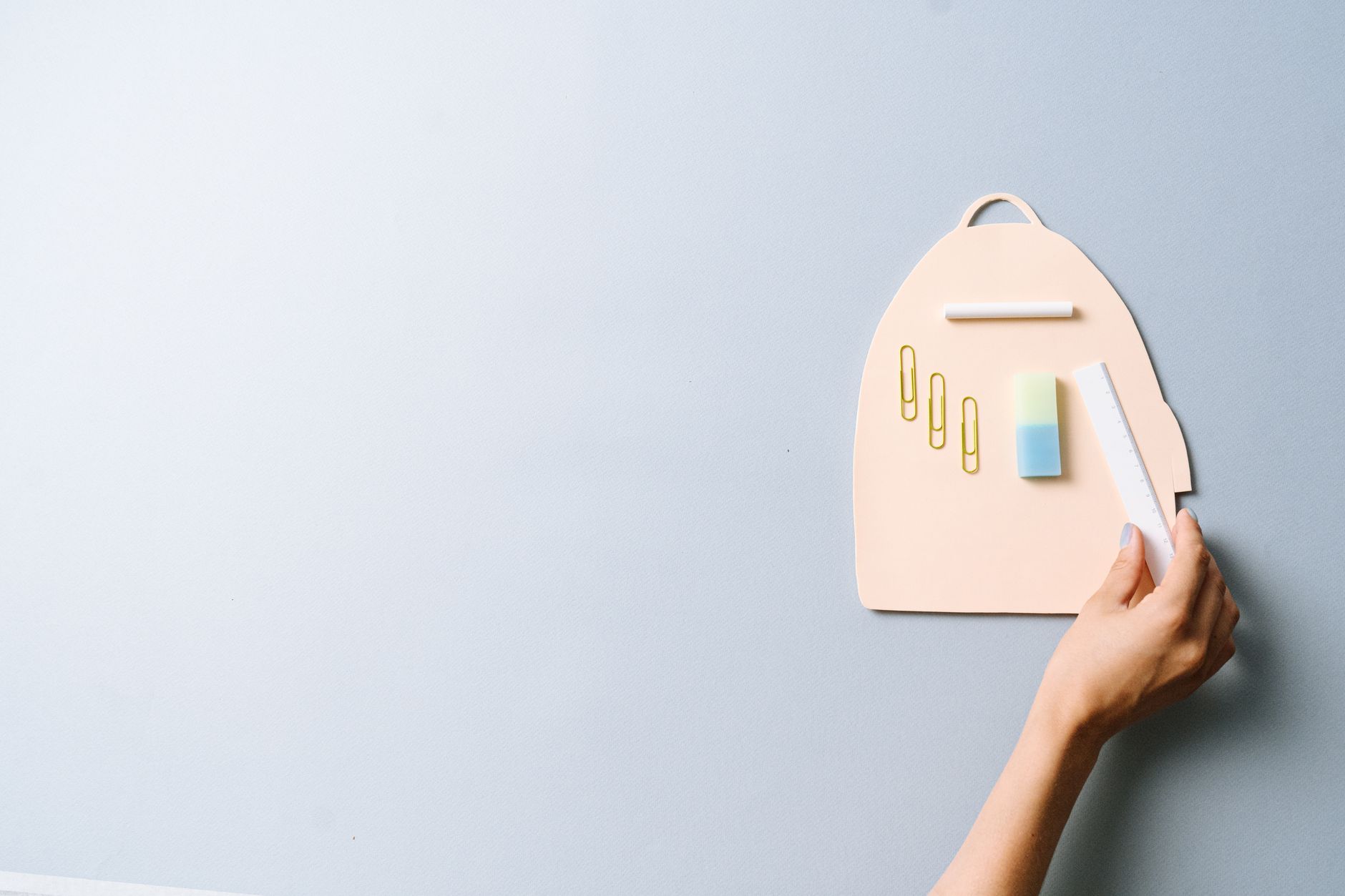 A minimalist flat lay of school supplies including a hand holding a ruler on a pastel background.