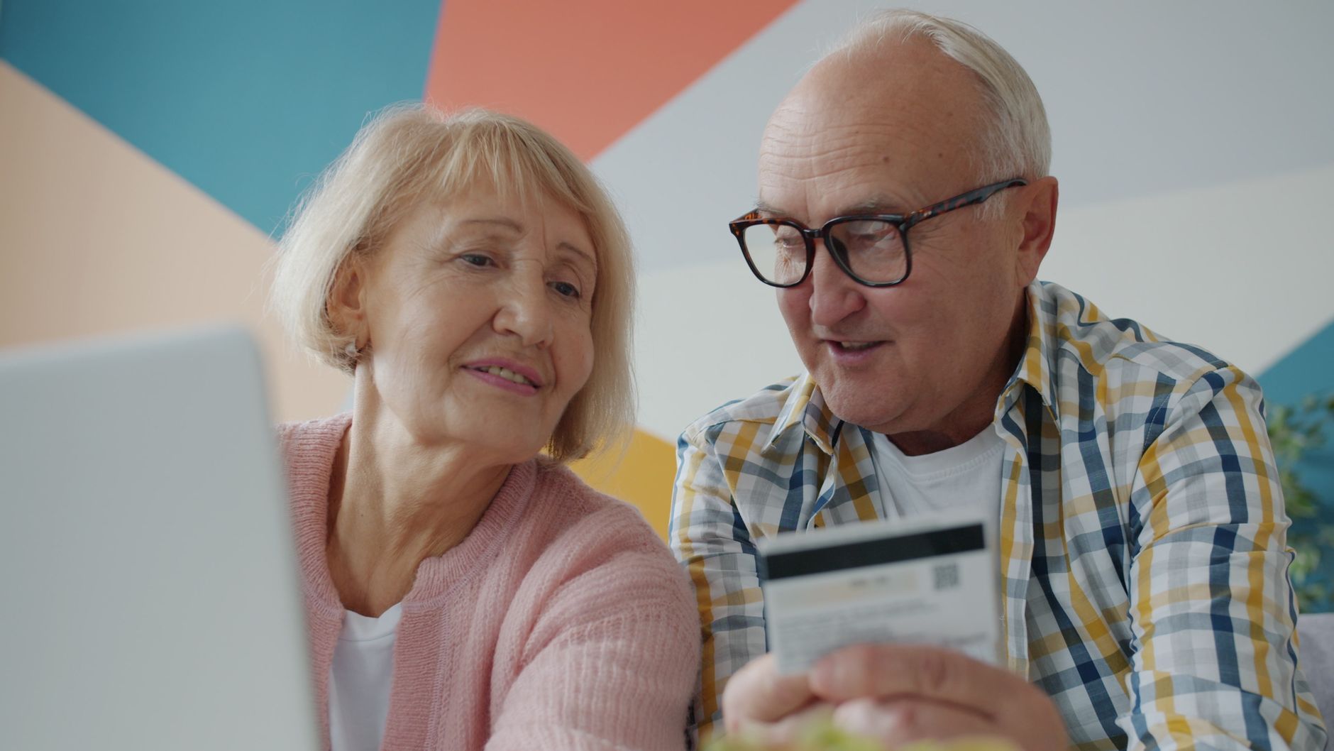 Senior couple using a laptop and credit card for online shopping at home, smiling and engaging.