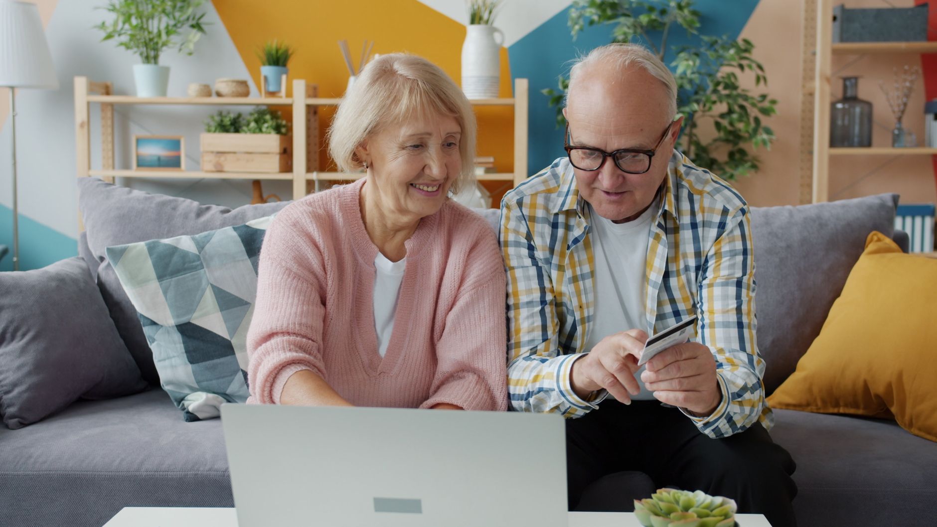 Elderly couple smiling while online shopping with a laptop and credit card.