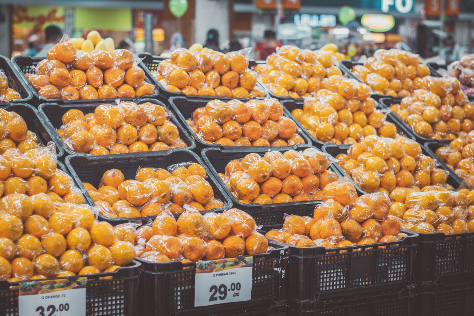Stack of fresh oranges wrapped in plastic at a grocery store, priced with tags.