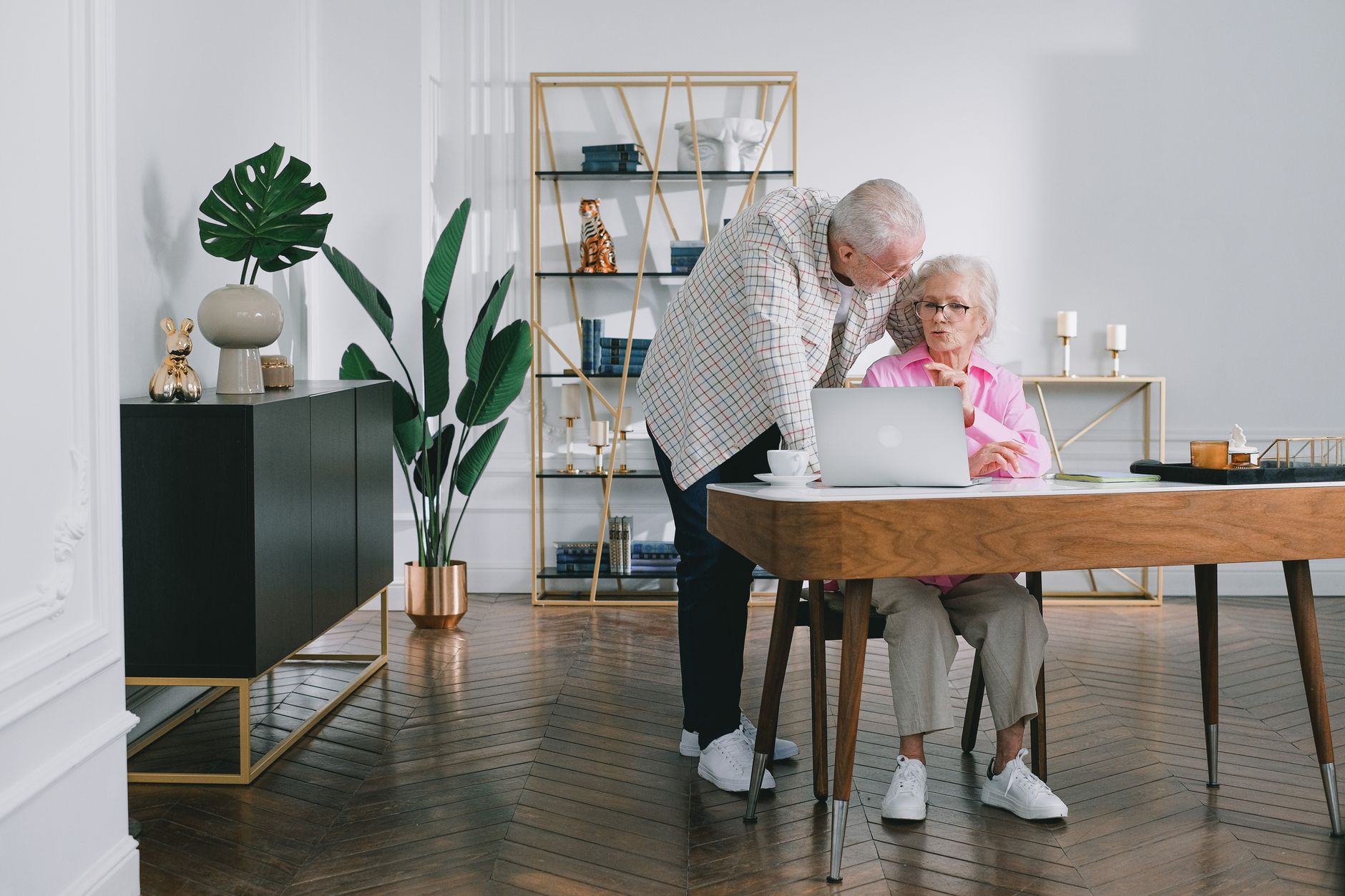 Senior couple using a laptop while discussing something in their modern living room.
