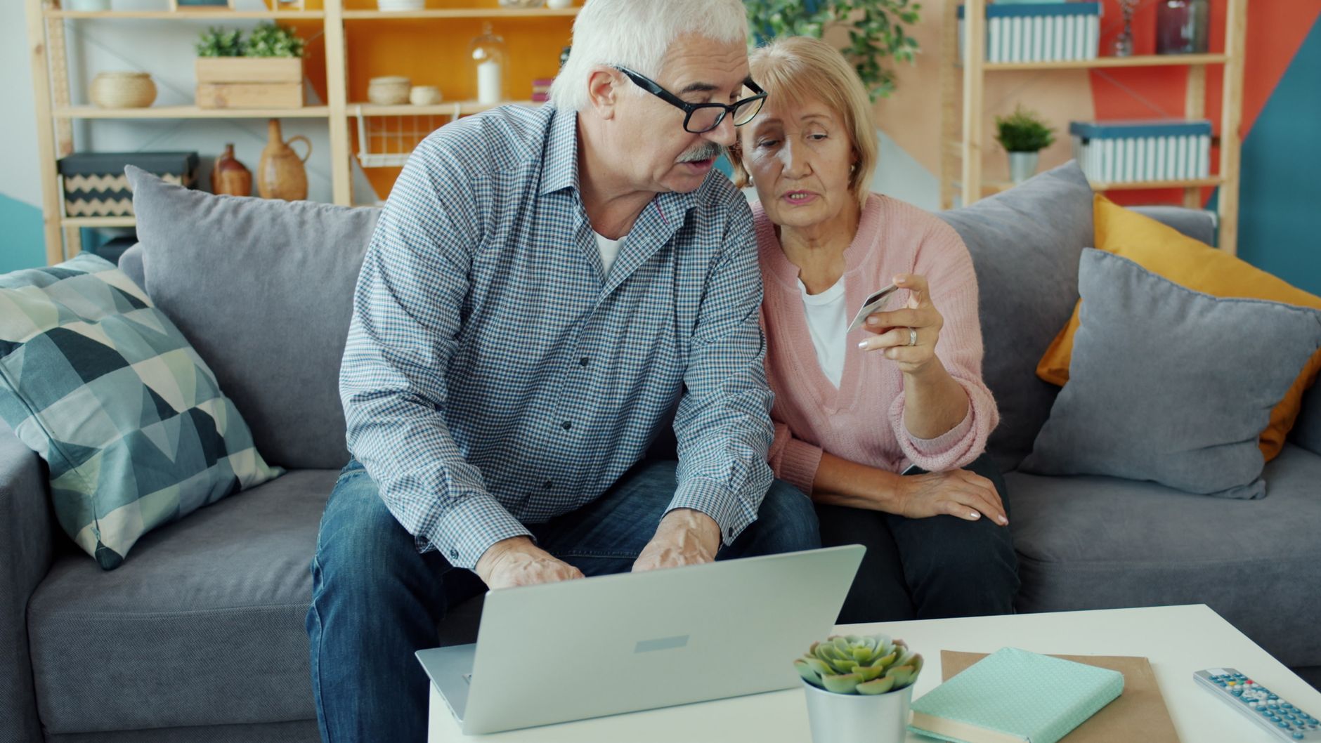 Elderly couple using a laptop and credit card in a cozy living room.