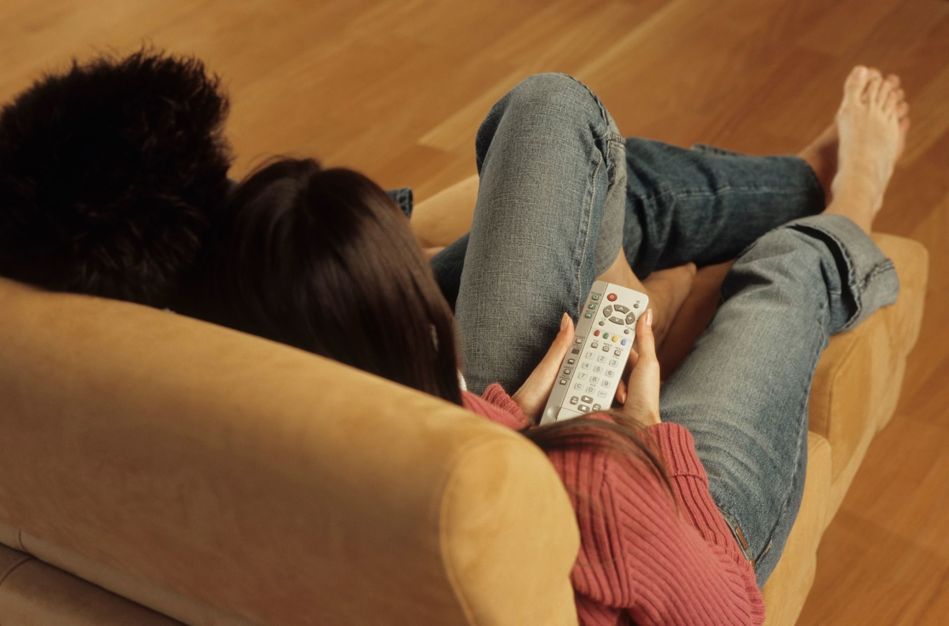 A couple relaxes on a couch holding a remote, enjoying a cozy indoor moment.