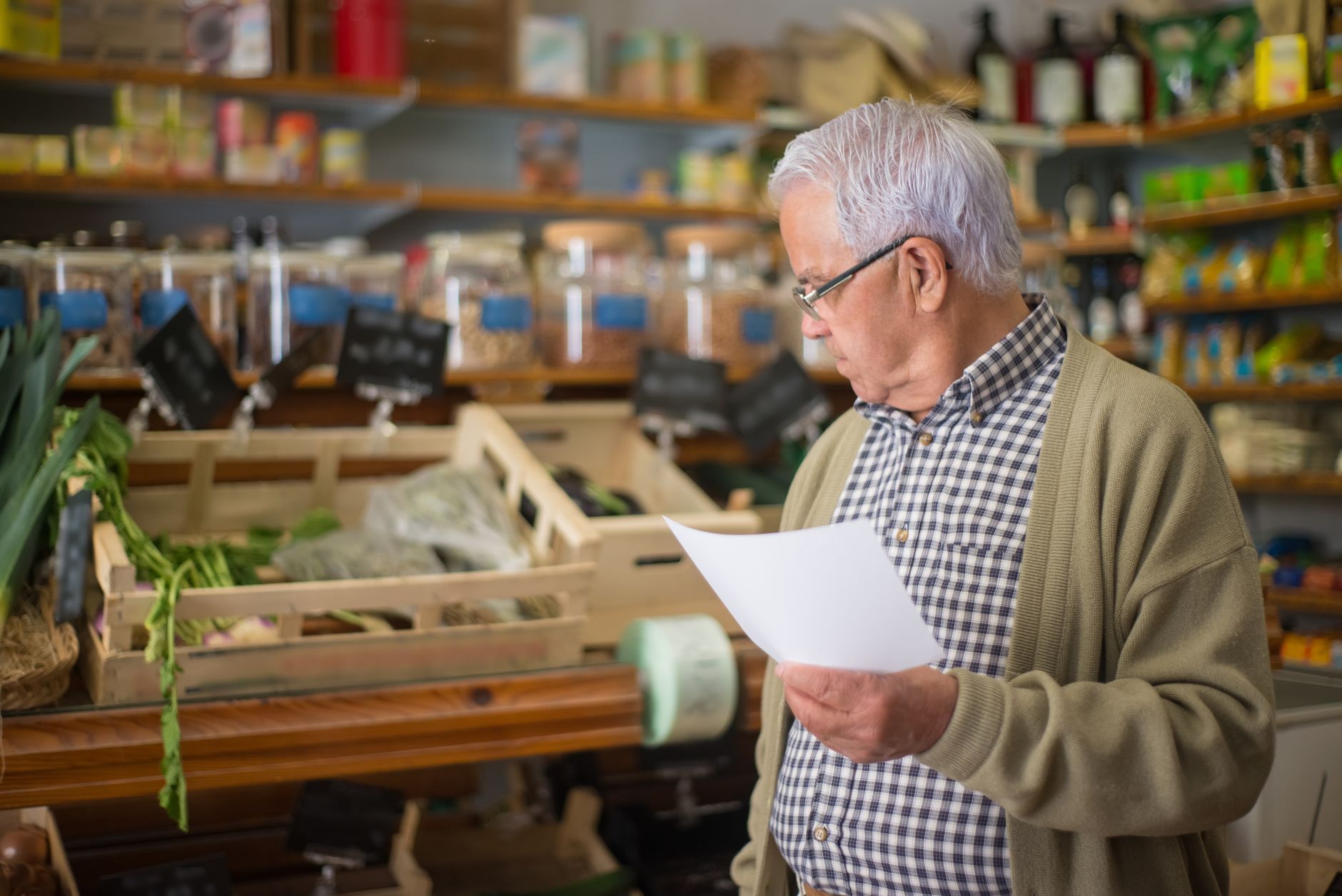Senior man shopping in a Portuguese store, holding a shopping list.